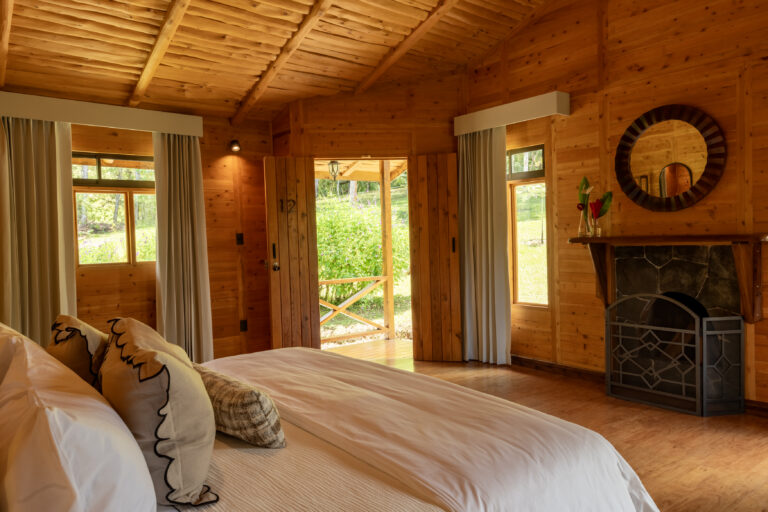 cozy cabin bedroom. through the open doorway you can see a porch and view of tropical greenery